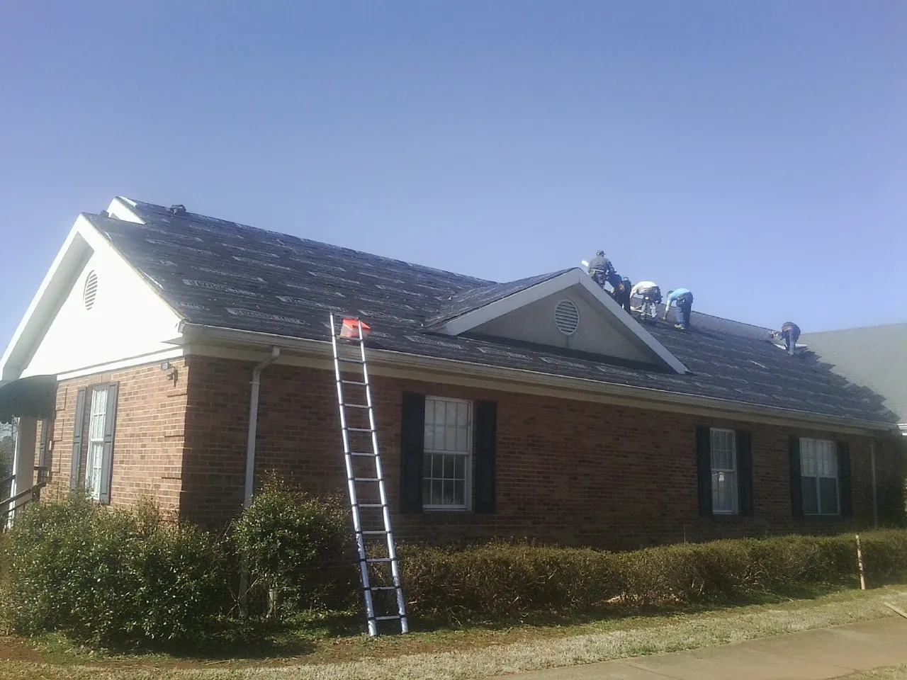 Crew tearing shingles off a brick ranch roof with a ladder set — Metal Roof Repair work by our crew in Cumberland Center