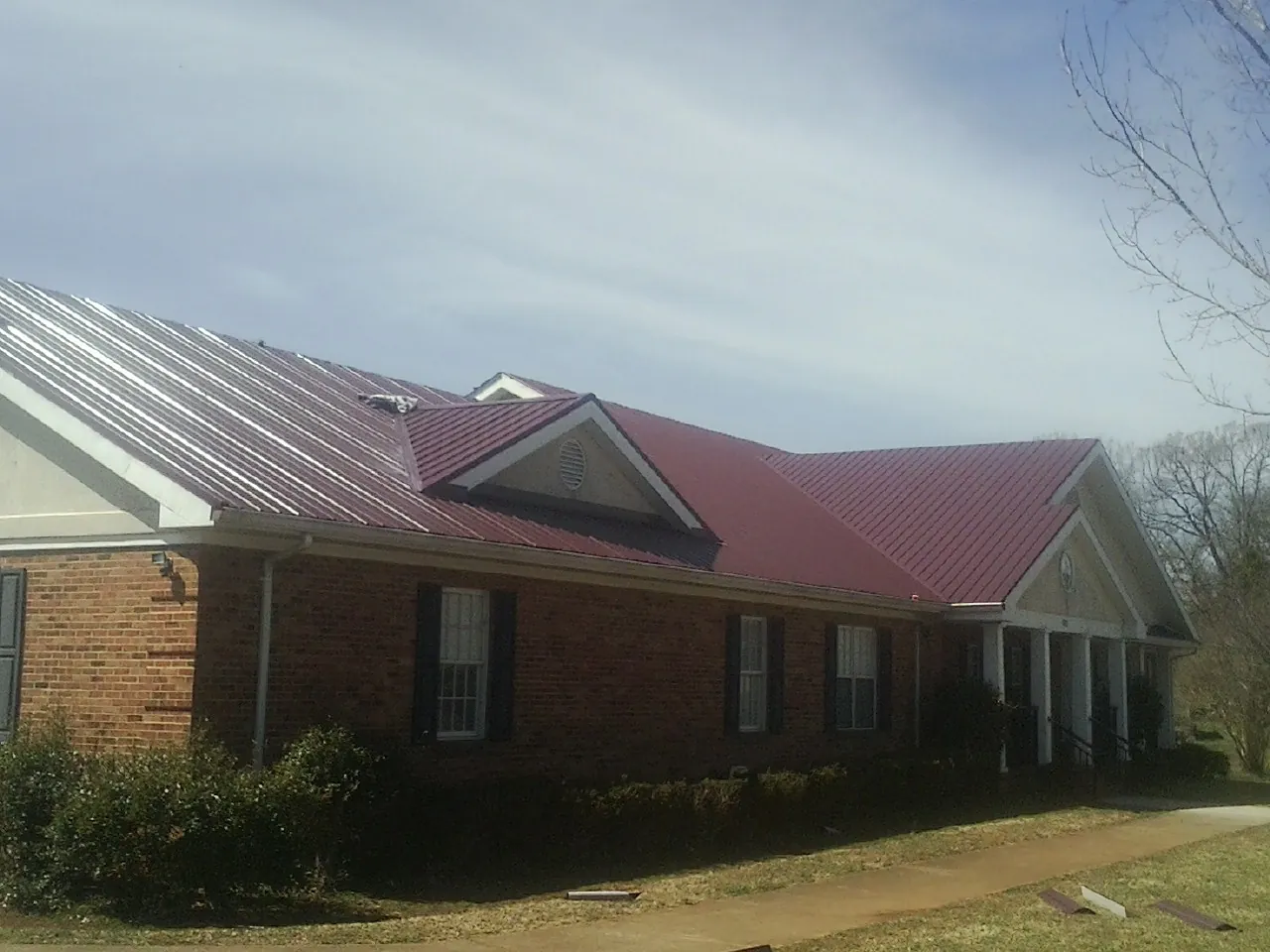 Red metal roof with gabled entries on a long brick building, from a Hail Damage Roof Repair job in Cumberland Center