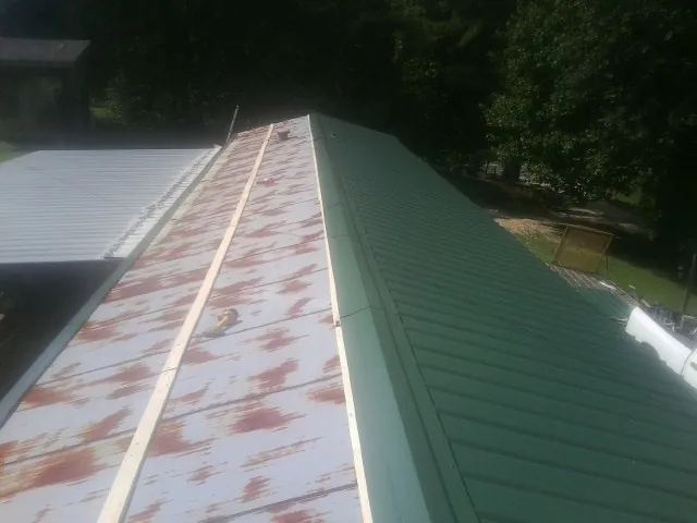 Old rusted panels beside newly installed green metal roofing — Wind Damage Roof Repair by Roofing Brothers in Cumberland Center
