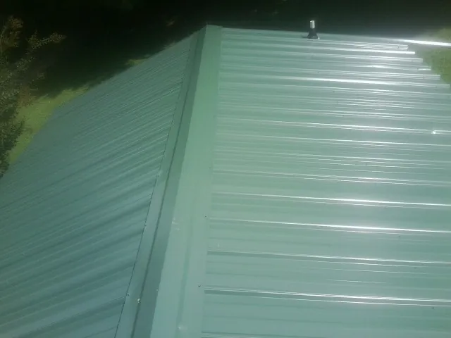 New green metal panels meeting at the ridge of a roof — Flat Roof Repair work by our crew in Cumberland Center