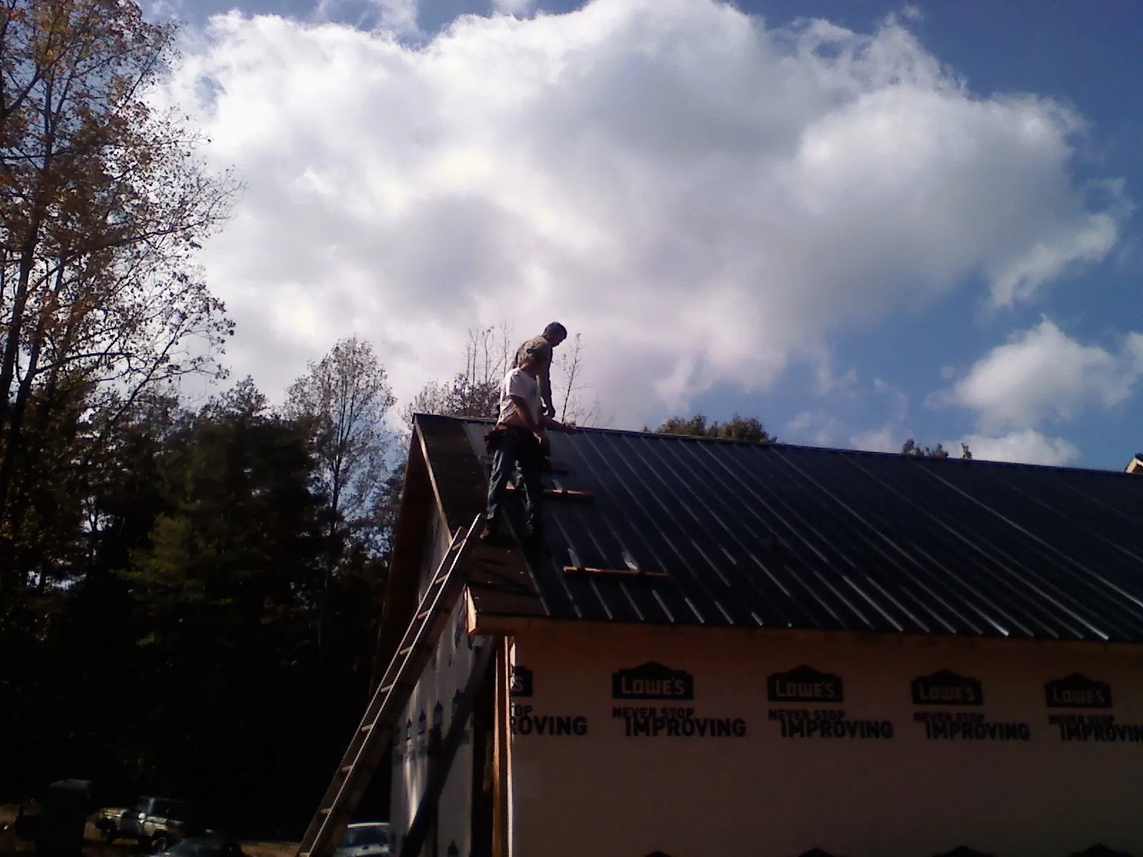 Roofer fastening dark metal panels high against a cloudy sky, from a Roof Inspection job in Cumberland Center