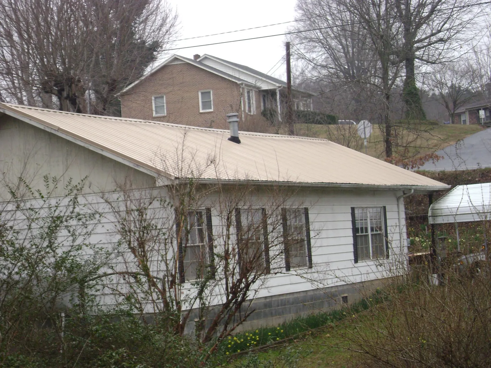 Tan metal roof on a white sided house set into a hillside in Cumberland Center