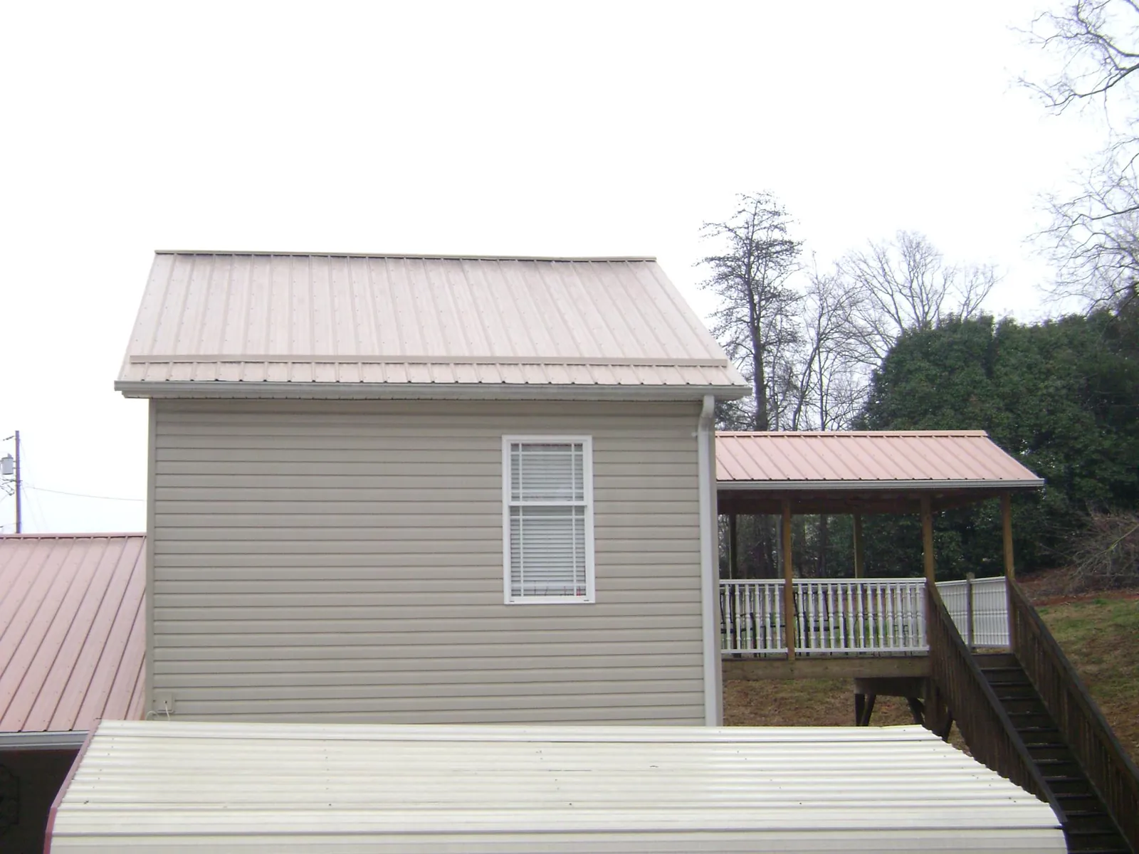 Tan metal roofs on a two story addition and attached porch, from a Roof Replacement job in Cumberland Center